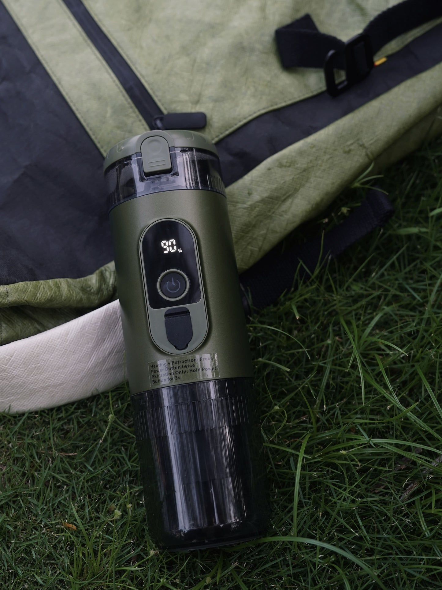 TrailBrew green portable espresso maker on grass beside green canvas travel bag