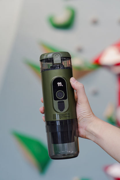 Hand holding TrailBrew green portable espresso maker at climbing gym showing compact handheld size