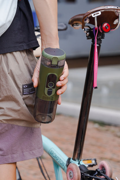 Hand holding TrailBrew green portable espresso maker beside a folding bicycle on urban street