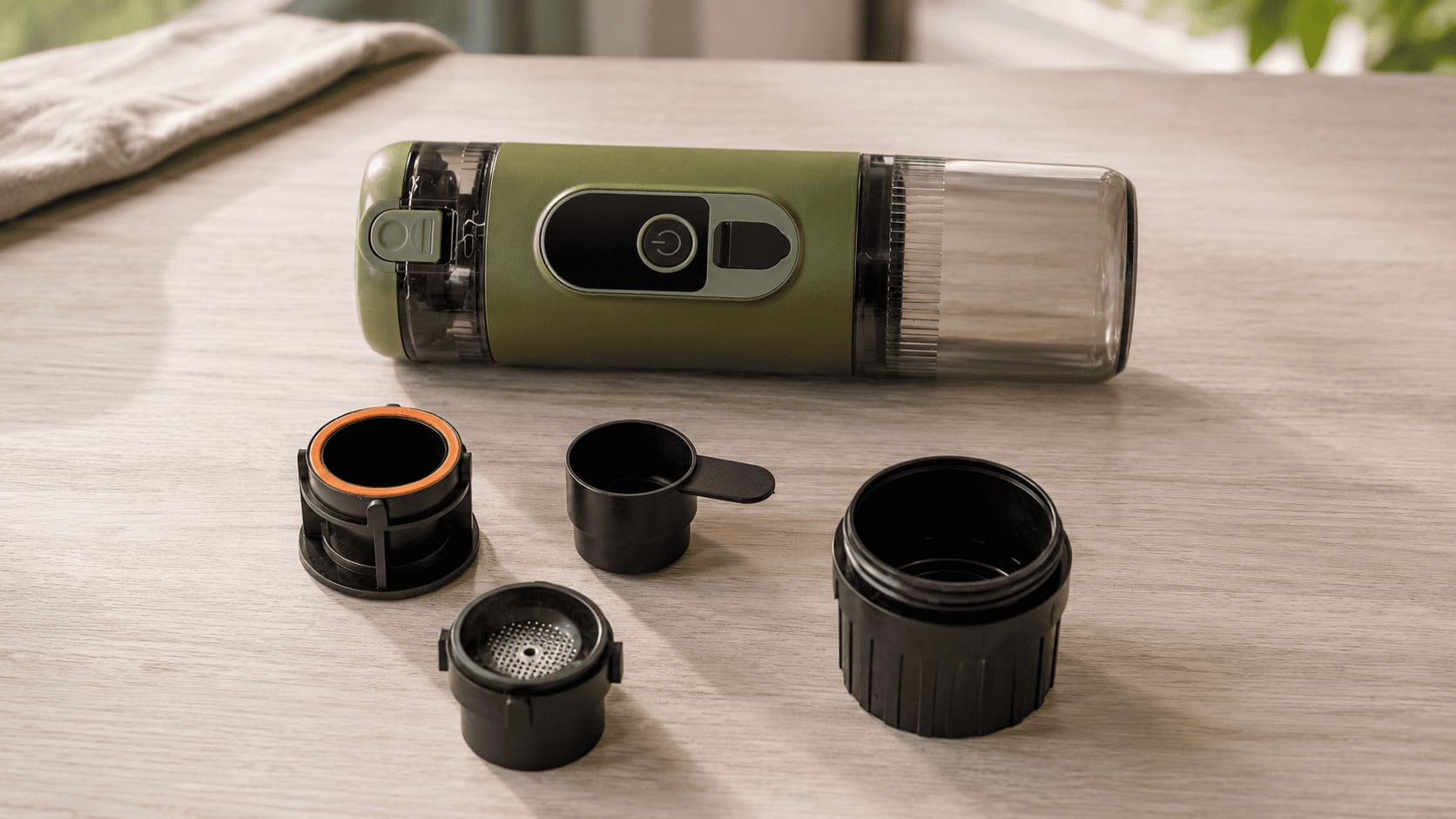 TrailBrew green portable espresso maker with three removable parts disassembled on wooden table